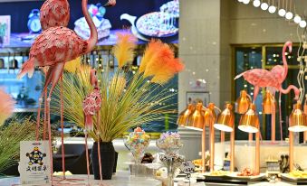 a pink flamingo statue stands in the center of a buffet , surrounded by various pastries and desserts at Phoenix Hotel