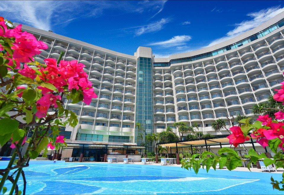 a large hotel building with a swimming pool in front of it , surrounded by lush greenery at Loisir Hotel Naha