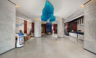 a large hotel lobby with a blue chandelier hanging from the ceiling , a reception desk , and several robots standing in front of it at Mianyang Booking Hotel