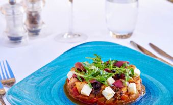 a blue plate with a dish of food on it , accompanied by two wine glasses and a fork at Te Moana Tahiti Resort