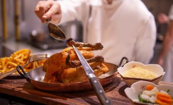 a man in a chef 's uniform is standing at a dining table , holding a spatula and preparing to carve a roasted chicken at L'Hotel de Beaune