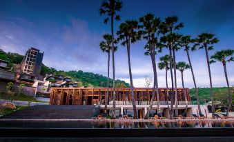 a modern building with wooden panels and palm trees , surrounded by a large pool and mountains at The Naka Phuket