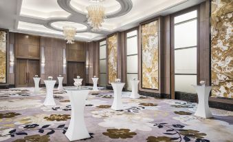 a modern , spacious room with white tables and chairs , gold accents , and large windows , decorated with a chandelier and flower patterns on the walls at Sheraton Can Tho