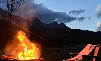 a man is relaxing in a chair near a campfire , surrounded by mountains and clouds in the background at The Rock Hotel