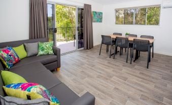 a modern living room with a gray couch , dining table , and sliding glass doors leading to an outdoor balcony at Big4 Gold Coast Holiday Park
