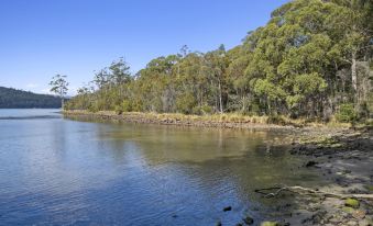 a calm body of water with trees on the shore and clear blue sky in the background at The Fox and Hounds Historic Hotel