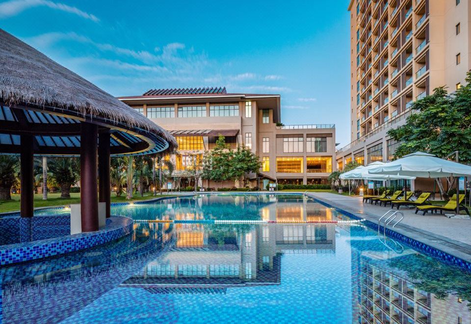 a large outdoor swimming pool surrounded by a hotel , with several people enjoying their time in the pool area at Sanya Xizang Hotel