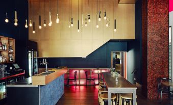 a modern restaurant with wooden tables and chairs , a blue counter , and pendant lights hanging from the ceiling at Saint Kilda Beach Hotel, an EVT hotel - Formerly Rydges St Kilda