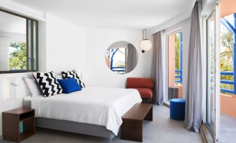 a large bed with a white comforter and black and white zigzag pillows is in a room with a blue chair , a wooden bench , at Salt of Palmar, Mauritius, a Member of Design Hotels