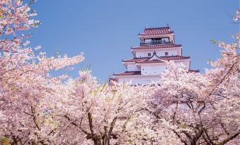 a castle - like building surrounded by a field of cherry blossom trees , creating a picturesque scene at Toyoko Inn Aizuwakamatsu Ekimae