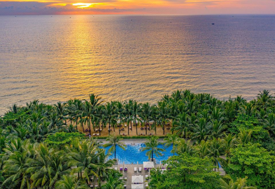a beautiful sunset over the ocean , with palm trees and a pool surrounded by chairs and tables at Salinda Resort Phu Quoc - Sparkling Wine Breakfast
