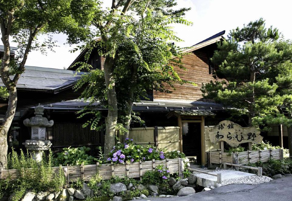 a small wooden building with a tree in front of it , surrounded by greenery and flowers at Ryokan Warabino