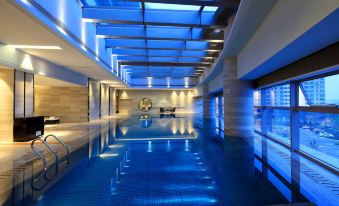 The interior showcases a spacious indoor pool with blue water and floor-to-ceiling windows offering views of the city at Grand Square Hotel Wuhu