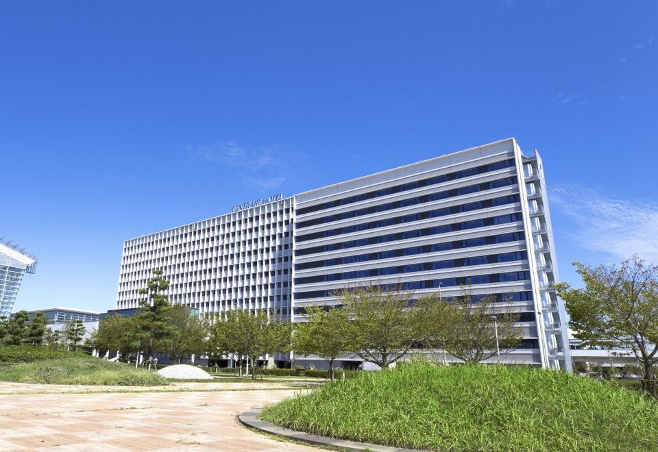 a modern office building surrounded by a grassy area and trees , with a clear blue sky in the background at Centrair Hotel