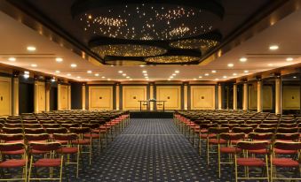 a large conference room with rows of chairs and a stage at the front , under a starry ceiling at President Hotel