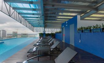 a large outdoor pool surrounded by lounge chairs , with a glass wall providing a view of the surrounding area at Citadines DPulze Cyberjaya