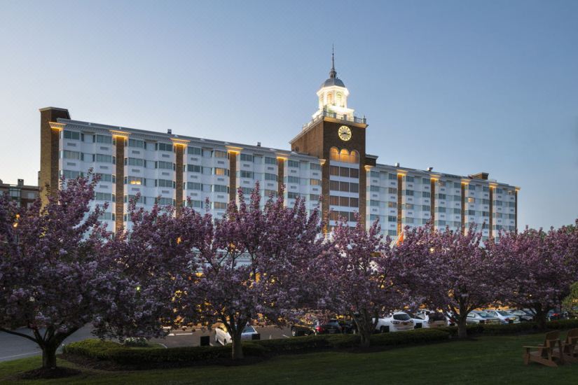 a large hotel building with a clock tower and multiple windows , surrounded by trees and flowers at Garden City Hotel