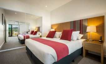 a modern hotel room with a large bed , white bedding , and red accents , along with other furniture at Quest Wodonga