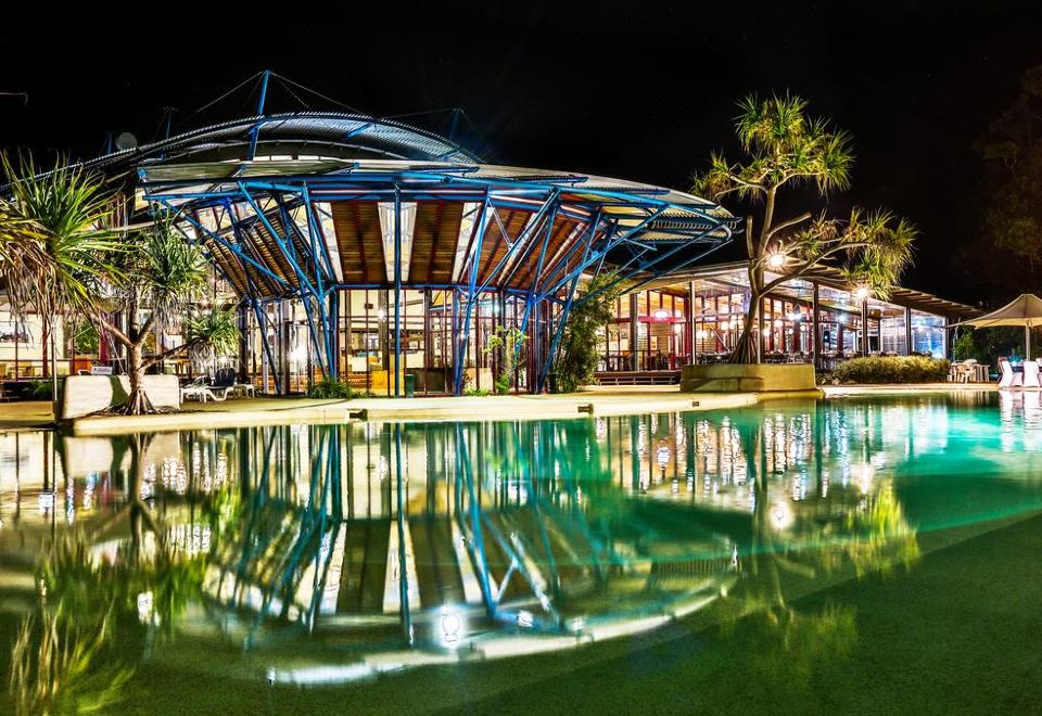 a large , modern building with a glass roof and surrounding trees is reflected in the water at Kingfisher Bay Resort