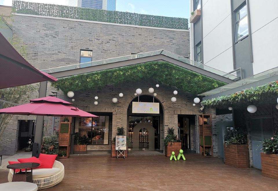 The entrance to a restaurant is covered, and there are tables and chairs on an outdoor patio in front at Campanile Shanghai Huaihai Hotel