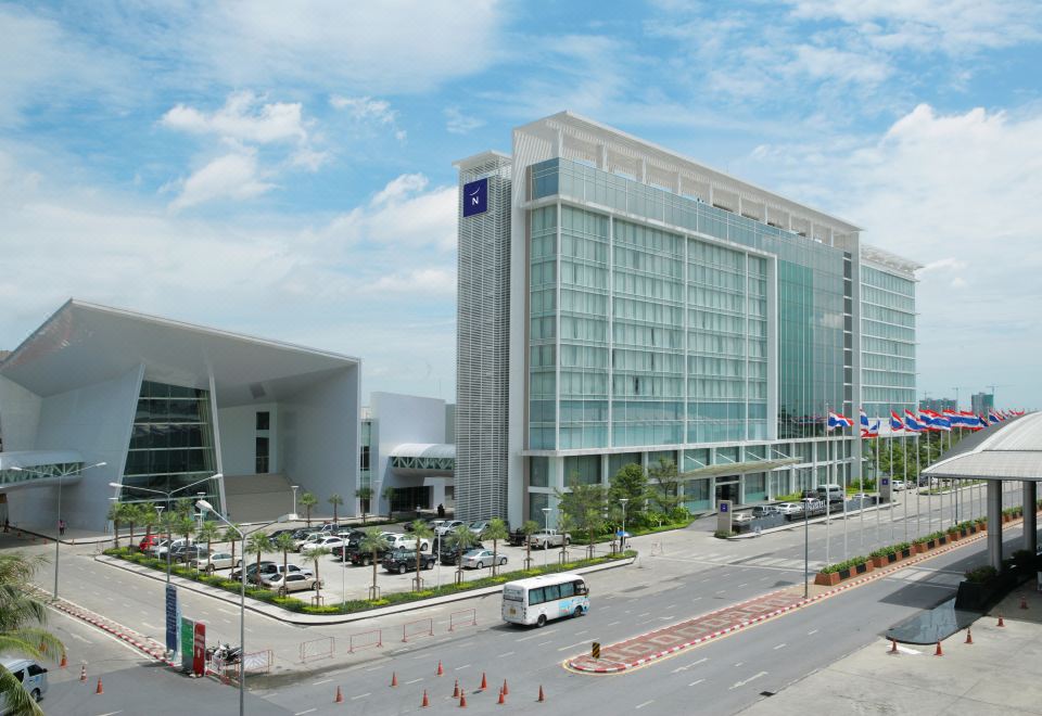 a large , modern building with a blue and white facade , surrounded by a city street at Novotel Bangkok Impact