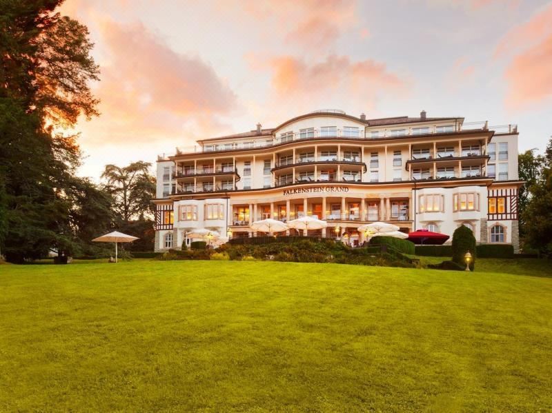 a large white hotel surrounded by green grass and trees , with a beautiful sunset in the background at Falkenstein Grand, Autograph Collection