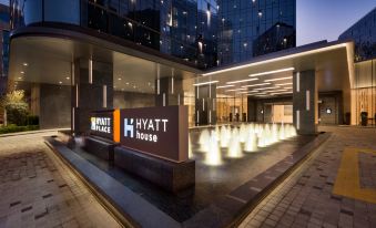 At night, a building is surrounded by tall trees and features two large vases in front at Hyatt Place Shanghai Hongqiao CBD