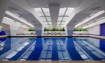 a modern swimming pool with blue water , surrounded by white walls and greenery , under a skylight at Hotel Royal
