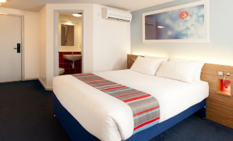 a neatly made bed with a colorful blanket and two pillows is in a room with blue flooring at Travelodge Norwich Central Riverside