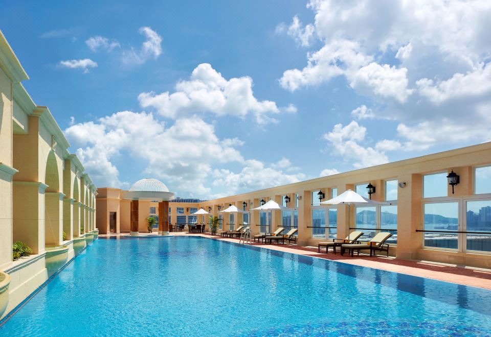 A large swimming pool with chairs and umbrellas is located next to the blue sky at The Royal Garden Hotel