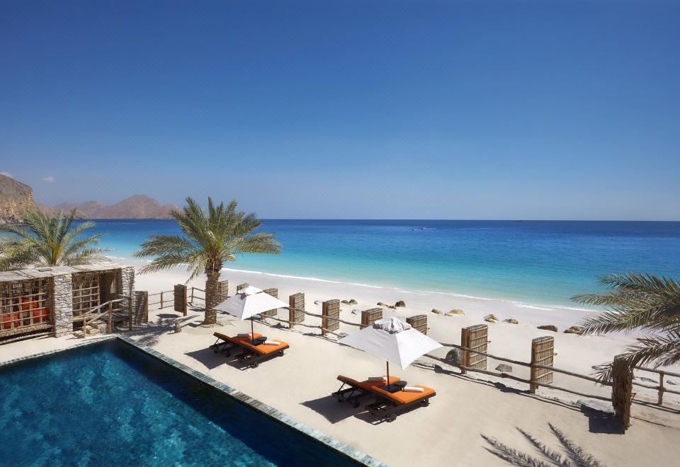 a beautiful beach resort with white sand , clear blue water , and a few lounge chairs on the sand at Six Senses Zighy Bay