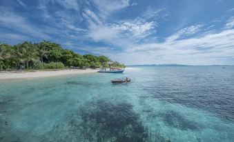 a boat is anchored in the clear blue water near a beach with trees and buildings at Gangga Island Resort & Spa