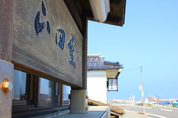 a wooden sign with blue chinese characters is attached to a building , overlooking the ocean at Yamadaya