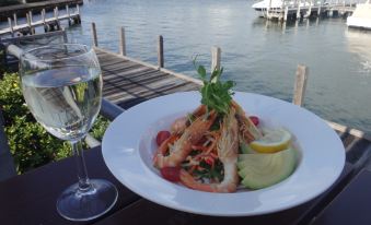 a white plate of food is on a table with a glass of wine and a view of water at Mandurah Quay Resort
