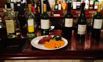 a plate of food and two bottles of wine are on a bar counter with bottles in the background at The Eight Bells