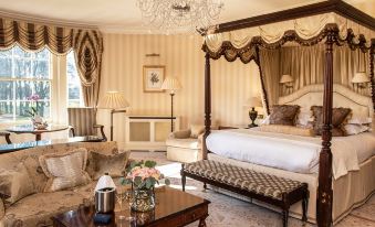 a luxurious bedroom with a large four - poster bed in the center , surrounded by various pieces of furniture and decorations at Lucknam Park Hotel