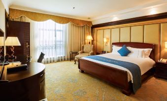 a large , well - made bed with a blue comforter is in the middle of a room with a window and a desk at City Hotel