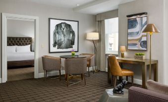 a hotel room with a dining table , chairs , and a painting on the wall , along with a bed and other amenities at Hilton Boston Park Plaza