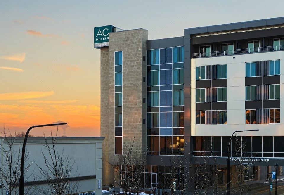 a modern building with a green logo on the side is set against a backdrop of a sunset at AC Hotel Cincinnati at Liberty Center