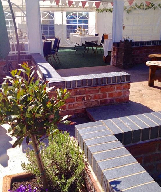 a patio area with a brick wall , wooden table and chairs , and a potted plant at St Quintin Arms