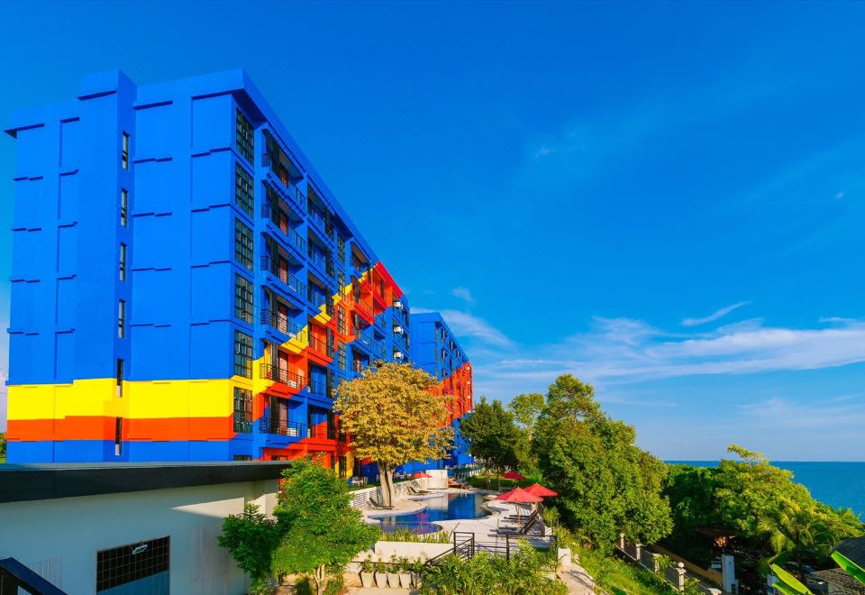 a large , colorful building with multiple floors and balconies is situated on a hillside overlooking the ocean at Play Phala Beach Rayong