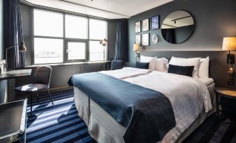 a large bed with blue and white linens is in a room with striped carpet and windows at Scandic Falkoner