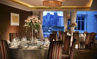 The dining room has large windows that provide a view of the city and is set up with tables for ten people at The Kowloon Hotel