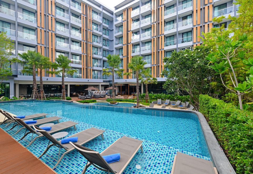 an outdoor swimming pool surrounded by a building , with several lounge chairs placed around the pool at Hotel Amber Pattaya