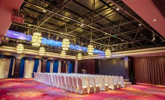 a large , empty conference room with rows of white chairs and blue curtains , under high ceilings and chandeliers at Mianyang Booking Hotel