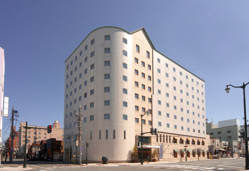 a large , modern building with a curved facade and many windows is situated on a street corner at Hotel JAL City Aomori
