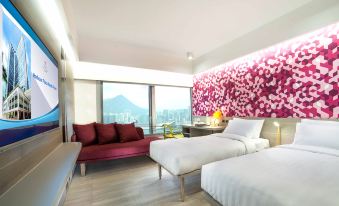 The room features two beds, an armchair, and a large window with a view of the city at night at Harbour Plaza North Point