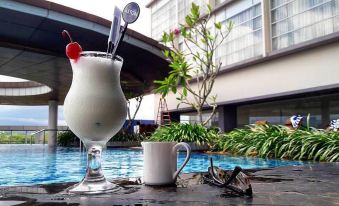 a cocktail with a straw and cherry garnish is next to a pool , next to a white cup at ASTON Purwokerto Hotel & Convention Center