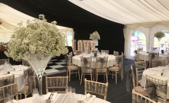 a well - decorated event space with white tables , black curtains , and a table centerpiece of white flowers at Coach House Hotel