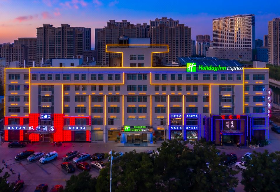 a large hotel with multiple floors and neon lights , surrounded by other buildings in the evening at Holiday Inn Express